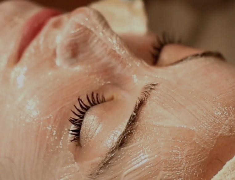 Esthéticienne tenant délicatement le visage d'une cliente pendant un soin du visage, cliente portant un bandeau de spa, chez Essbé Beauté